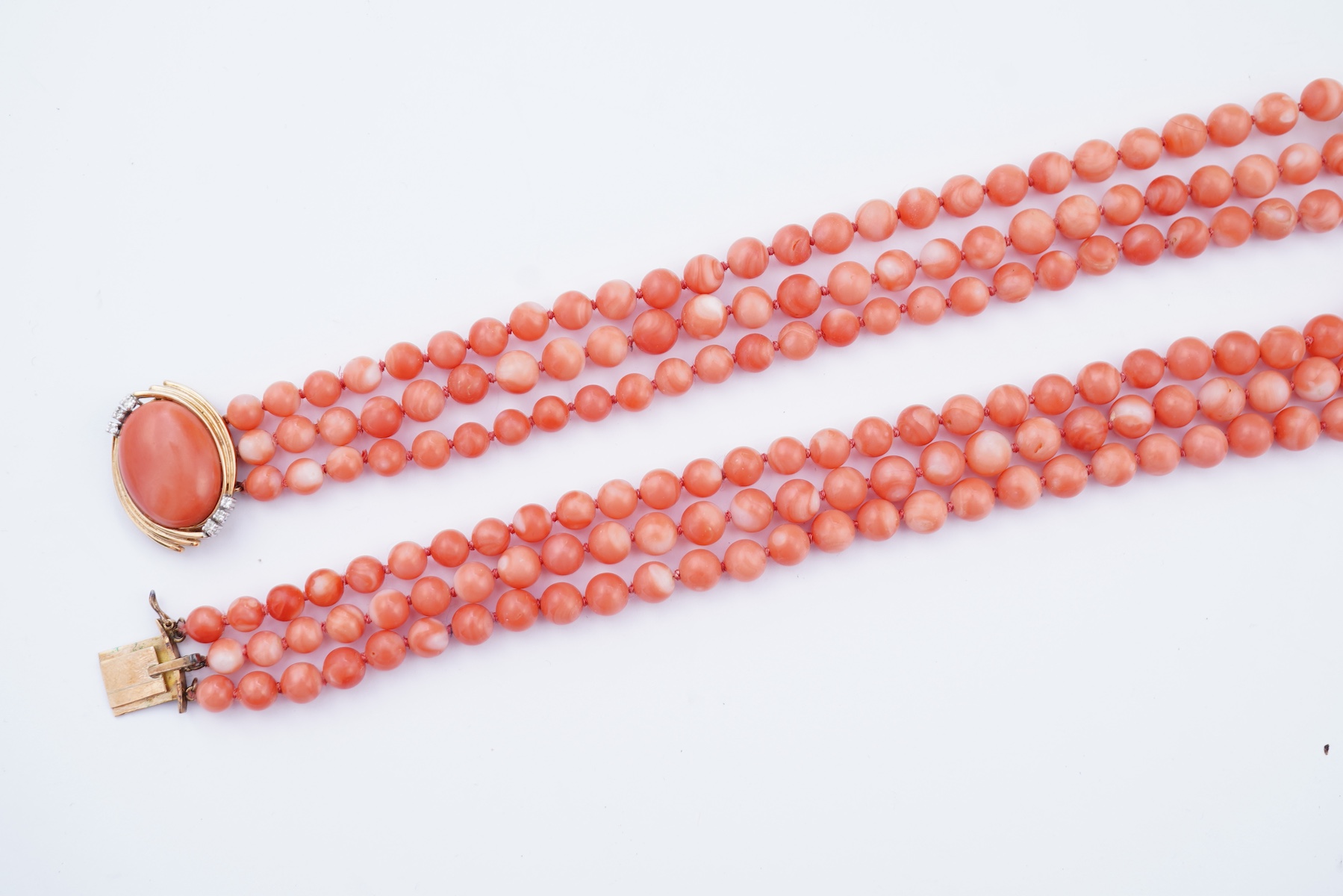 A coral necklace, composed of three strands of coral beads measuring approximately 5.1-6.6mm diameter, to a gold clasp set with a coral cabochon and brilliant-cut diamonds, mounted in gold, length 45.5cm, stamped 14K, ca